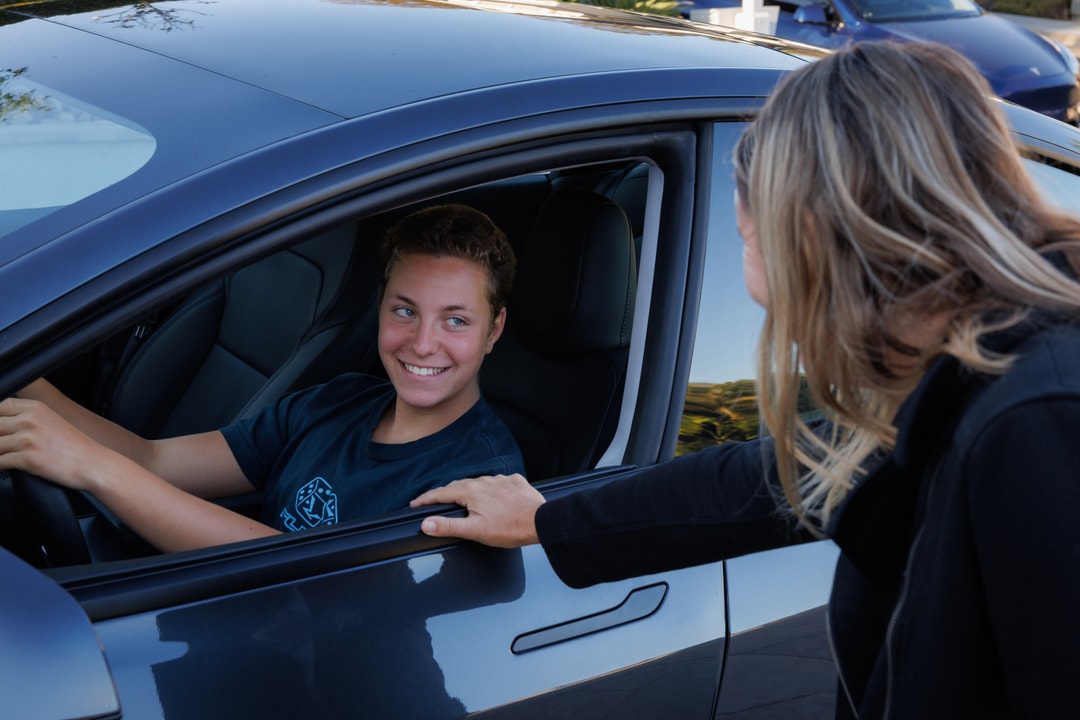 Teen driver in a vehicle speaking with a parent beside the car