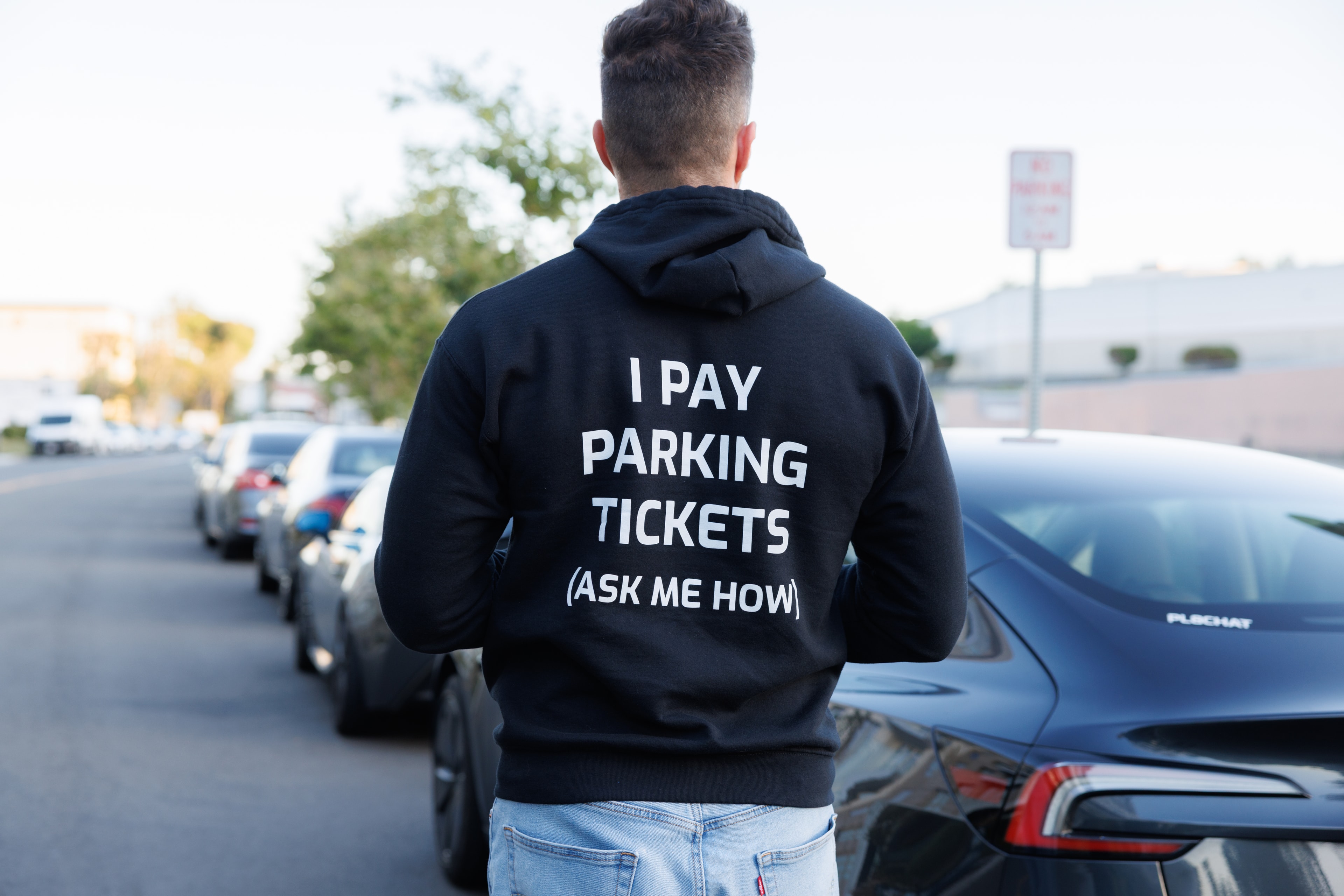 Person wearing 'I Pay Parking Tickets (Ask Me How)' hoodie next to a PL8CHAT car